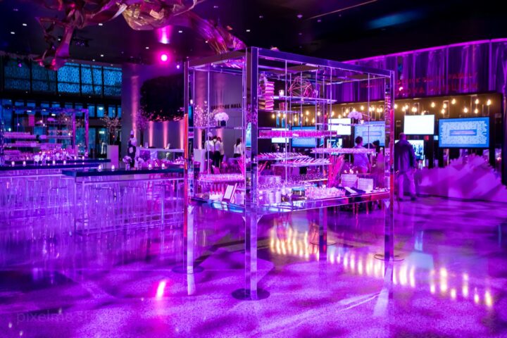 A dimly lit room with a purple ambiance, featuring a bar and tables for patrons to gather and socialize.