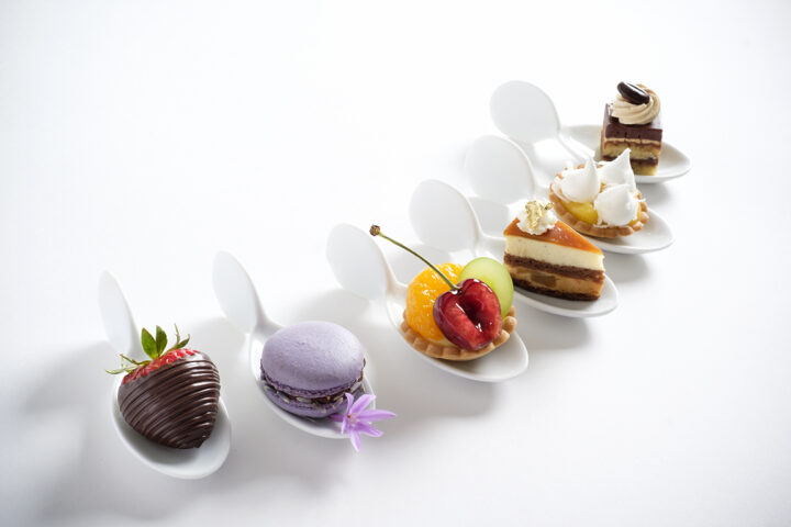 A row of bite-sized desserts on spoons, showcasing a variety of flavors and textures.